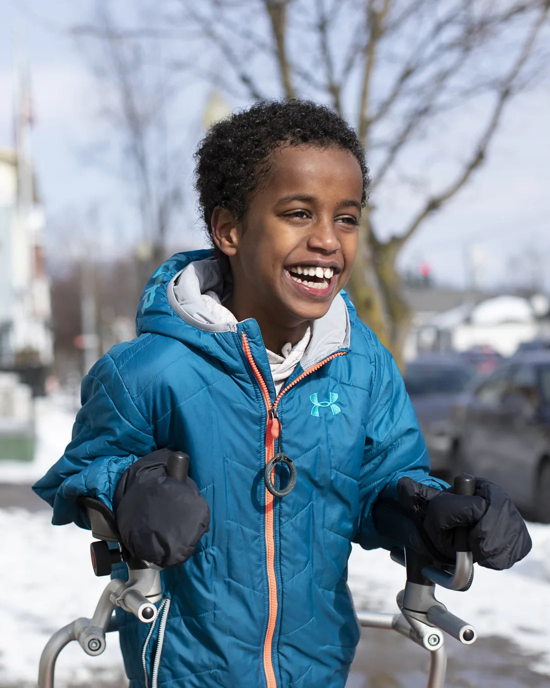A boy laughing out loud on a snowy sidewalk, his jacket zipped up with a MagZip and a big pull ring