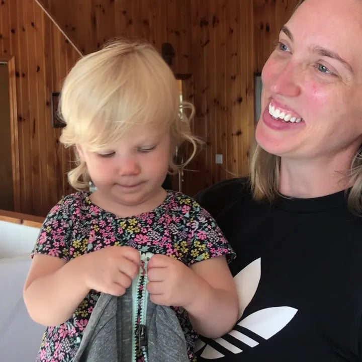 A mom watches her toddler zip her own hoodie