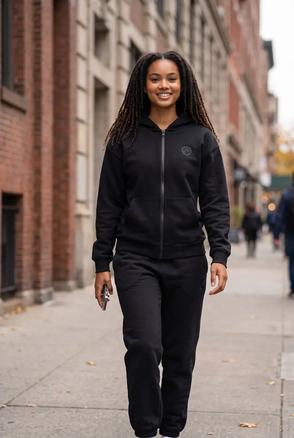 A woman in the black FREEDOM Hoodie and Jogger on a city sidewalk